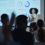 Woman, finance and applause with presentation by charts for stats, growth or review of sales with audience. Person, African presenter and results on graph, speech or projector for cheers at tradeshow